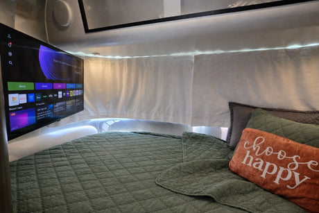 RV rental bedroom featuring a smart TV, comfy green bed with "choose happy" pillow, and warm LED lighting.