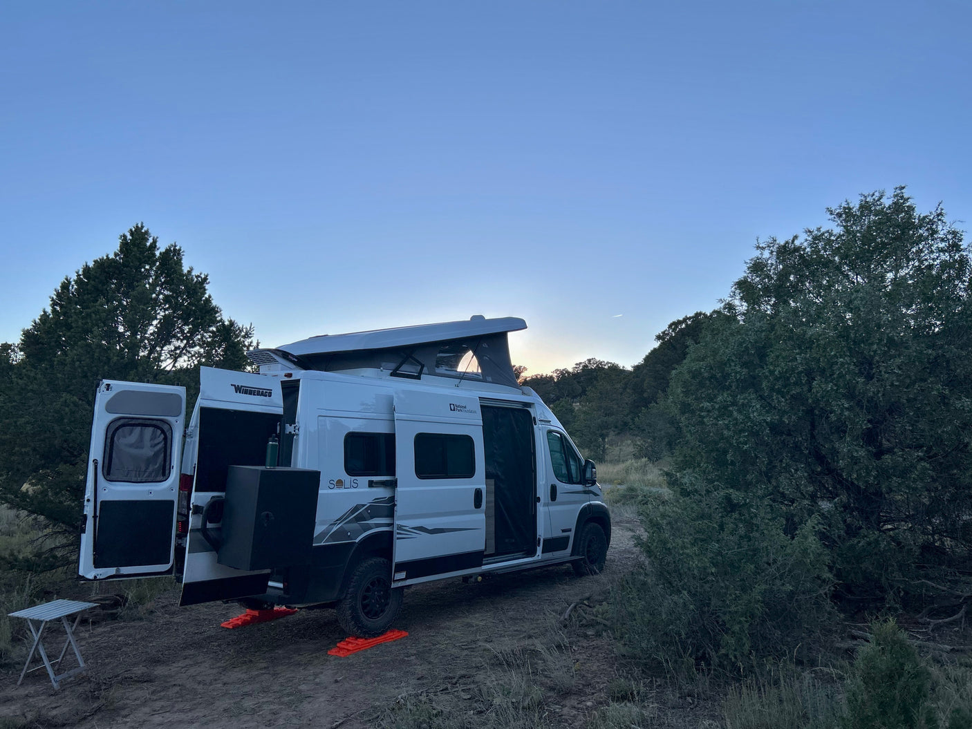 Scenic RV rental: White Winnebago Solis camper van parked with pop-top raised for a peaceful outdoor camping trip.