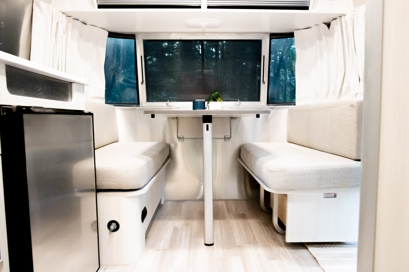 This inviting RV rental interior features a bright dinette with facing benches, a table, and windows looking out to nature.