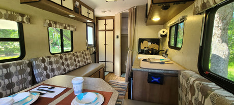 This RV rental interior features a cozy dining booth, equipped kitchen, and bathroom access, ready for road trips.