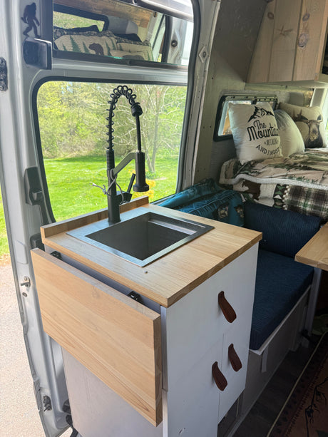 Cozy RV rental interior: custom camper van kitchen with sink, flexible faucet, wood counter, and mountain-themed decor.