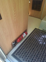 RV rental interior: A red fire extinguisher is secured to a light wood wall, beside a textured floor mat.