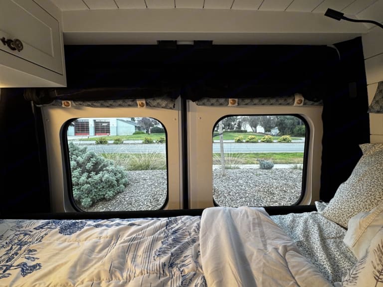 Cozy RV rental interior with bed and windows showing the outside. Perfect for van life adventures.