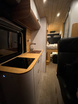 Modern RV rental interior featuring a bamboo kitchen with sink/cooktop and a cozy rear bed area, perfect for travel.