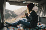 A person enjoys coffee and stunning mountain views from their cozy RV rental. The perfect van life adventure awaits!