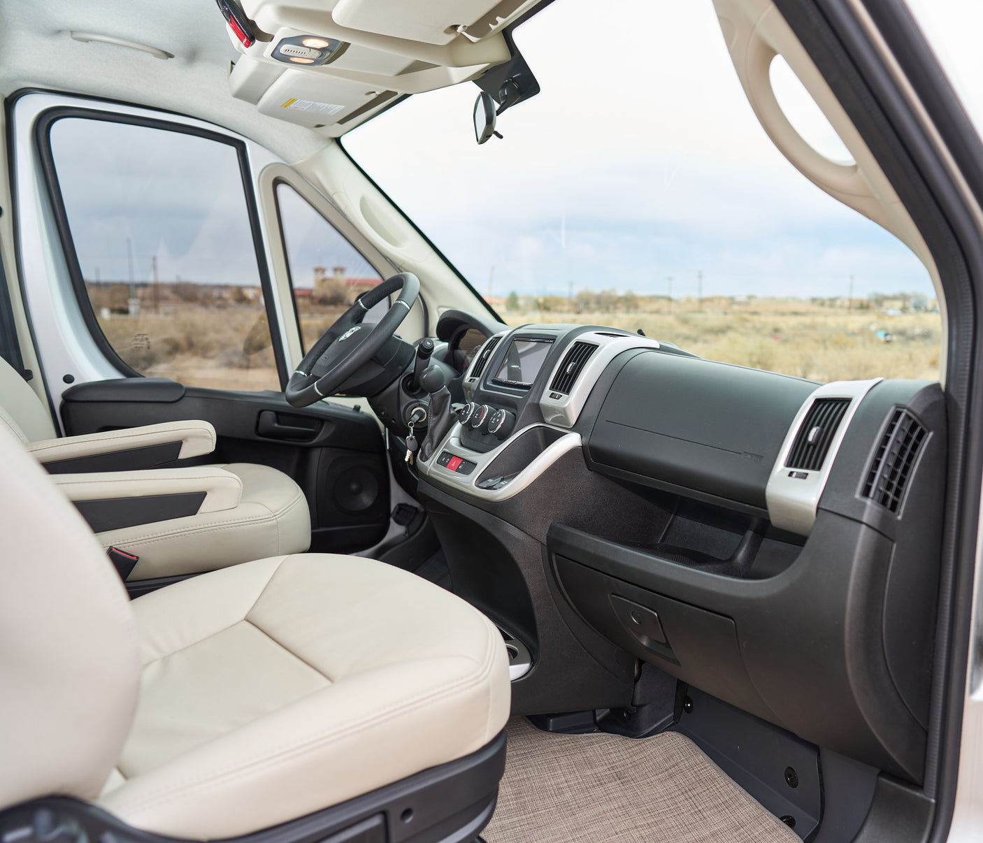 Step into this comfy rv rental. View of cream seats, driver's dashboard, and the open road ahead through the windshield.