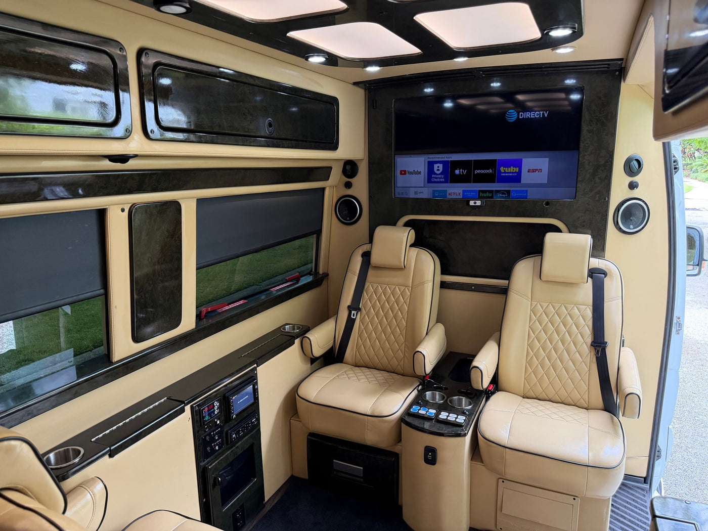 Luxurious RV rental interior shows plush tan seats, large entertainment screen, and custom controls for a comfortable journey. — photo 13