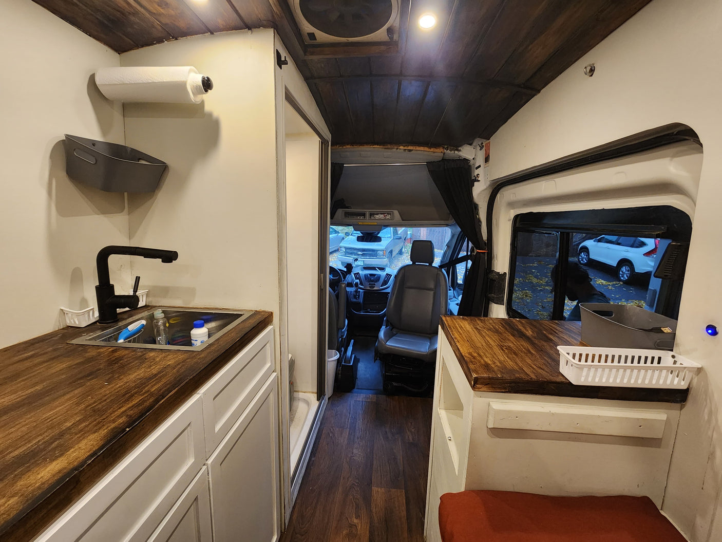RV rental with a warm wooden interior. Features a compact kitchen with sink, white cabinets, and driver's area.