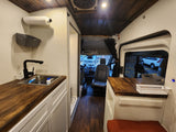 RV rental with a warm wooden interior. Features a compact kitchen with sink, white cabinets, and driver's area.