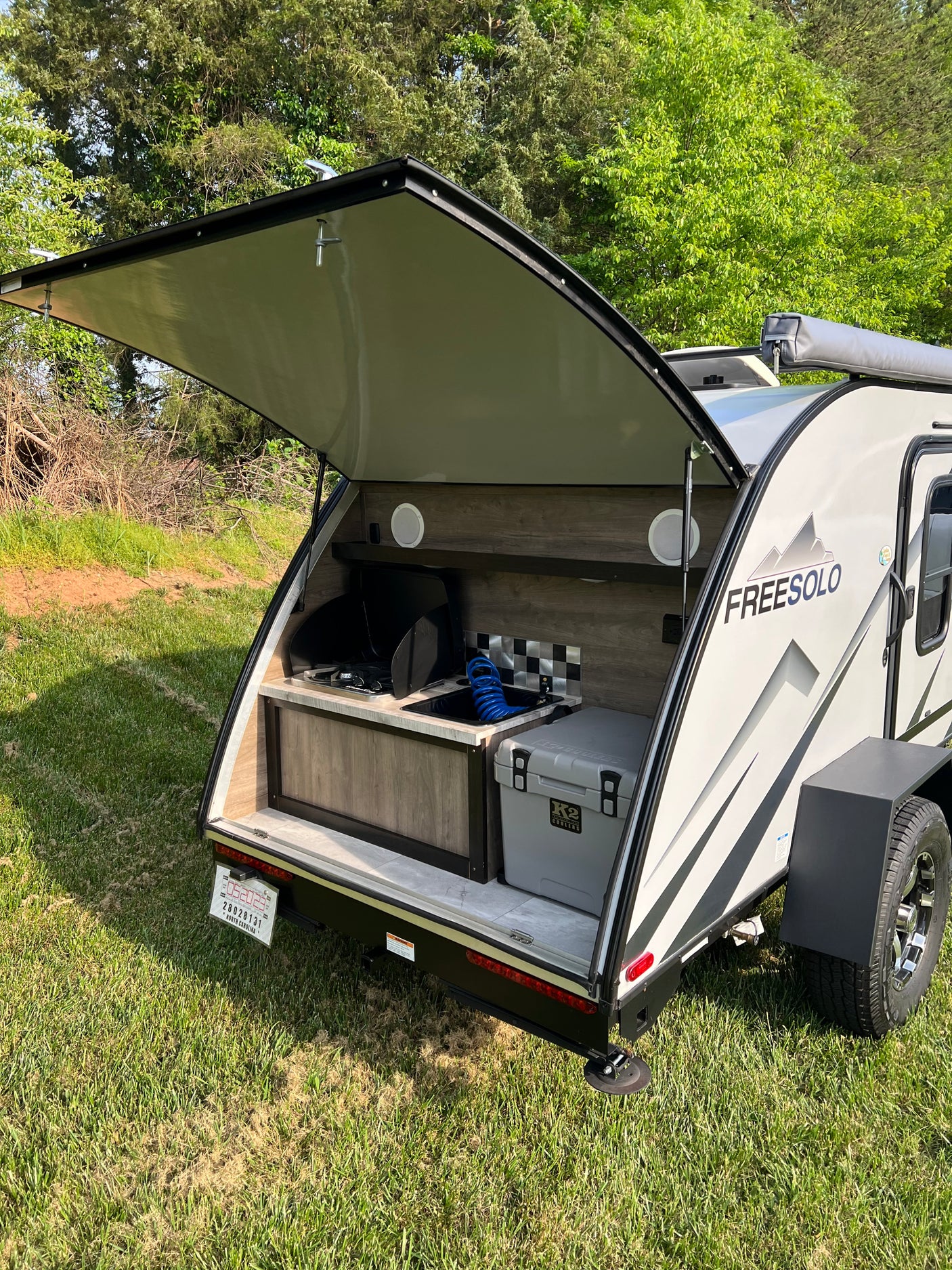 RV rental: A teardrop camper with its rear outdoor kitchen open, revealing a stove, sink, and cooler, set for camping.