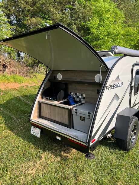 RV rental: A teardrop camper with its rear outdoor kitchen open, revealing a stove, sink, and cooler, set for camping.