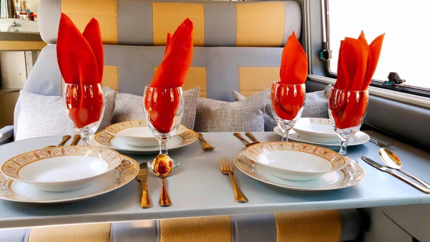 Experience comfortable dining in your RV rental with this elegant setup: four place settings, gold-rimmed plates, red napkins. — photo 13