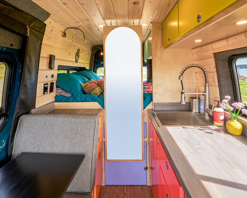 Spacious and modern RV rental interior, showcasing a compact kitchen, comfy bed, and versatile dining area in a wood-paneled camper van. — photo 18