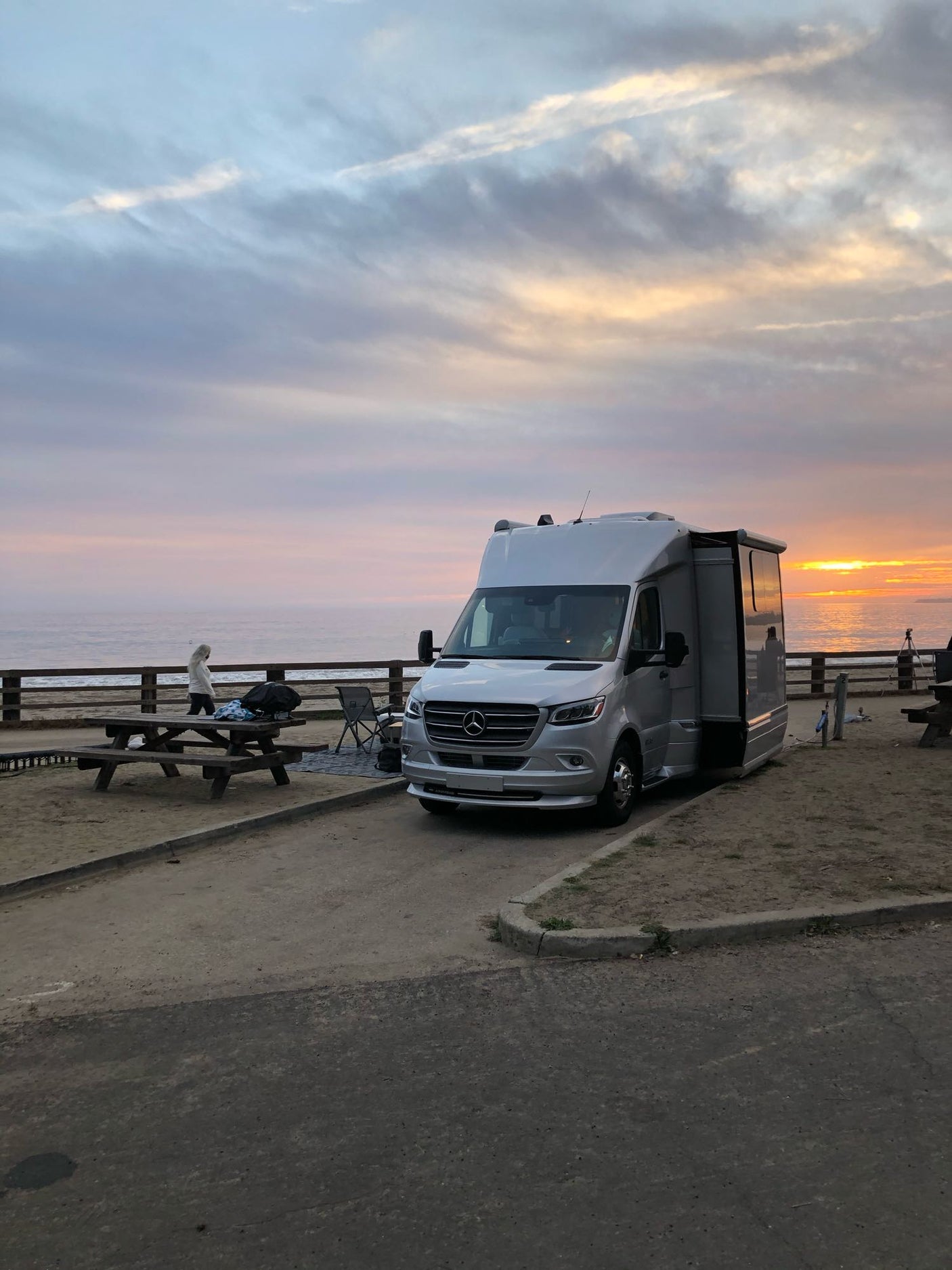 Stunning sunset over the ocean with a silver RV rental parked at a campsite, offering a serene coastal view.