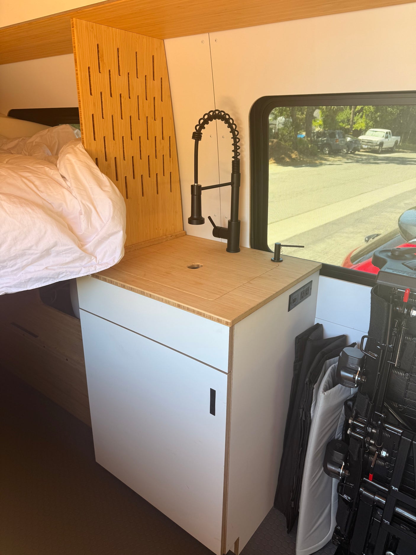 Cozy RV rental interior with a bed, bamboo kitchen countertop, modern black faucet, built-in storage, and a bright window.