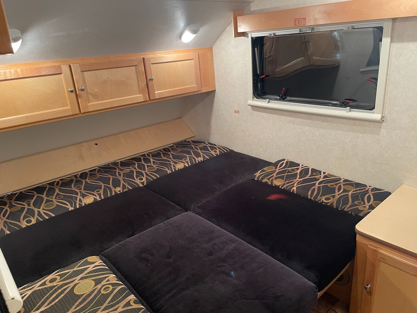 RV rental: Compact interior with a multi-cushion bed, overhead wood cabinets, and an exit window.