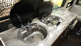 RV rental camper van kitchenette: chrome sink, two-burner stove with black covers, and patterned countertop for compact cooking.