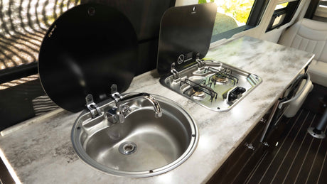 RV rental camper van kitchenette: chrome sink, two-burner stove with black covers, and patterned countertop for compact cooking.