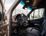 Inside an RV rental's driver's cabin: dashboard, steering wheel with accessibility hand controls, and palm trees visible outside.
