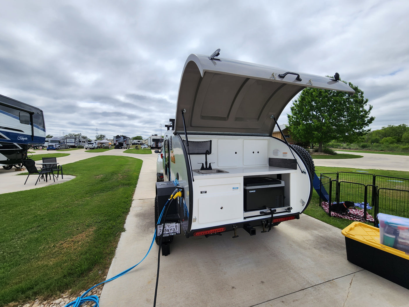 This RV rental teardrop camper offers a rear outdoor kitchen, perfect for camping. Parked at an RV site with a dog enclosure.