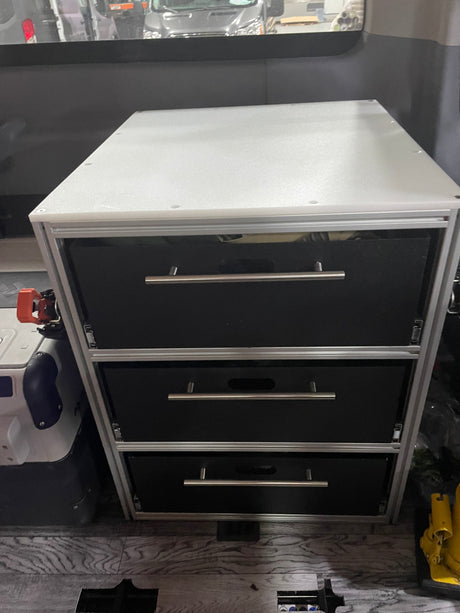 Compact custom drawer storage unit with three black drawers and silver handles, ideal for an RV rental interior.