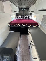 Modern rv rental interior: compact living with a cozy bed, white cabinets, and sleek gray accents.