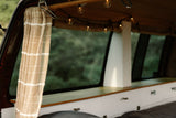 Inside a cozy RV rental: warm string lights, a light curtain, wood details, and a large window overlooking green nature.