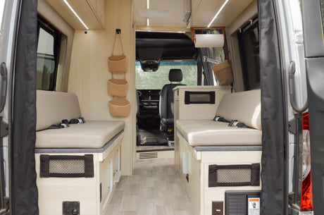 View of a modern rv rental interior: light wood, cushioned bench seats with seatbelts, and storage solutions.