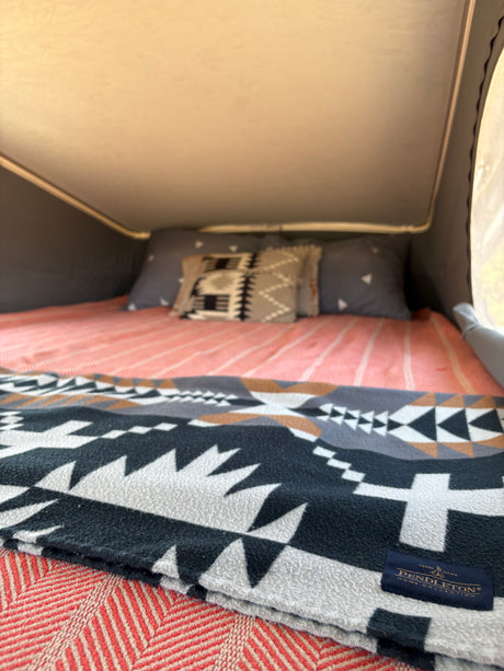 Comfortable RV rental bed with Pendleton blanket & pillows in a pop-top camper.