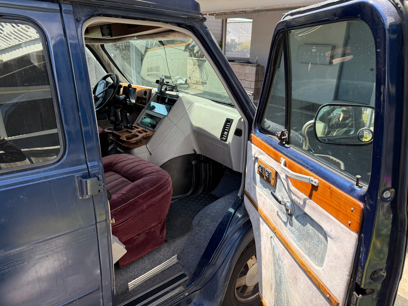 Open driver's door of a blue rv rental reveals a retro interior, including a red velvet seat and custom wooden console.