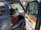 Open driver's door of a blue rv rental reveals a retro interior, including a red velvet seat and custom wooden console.