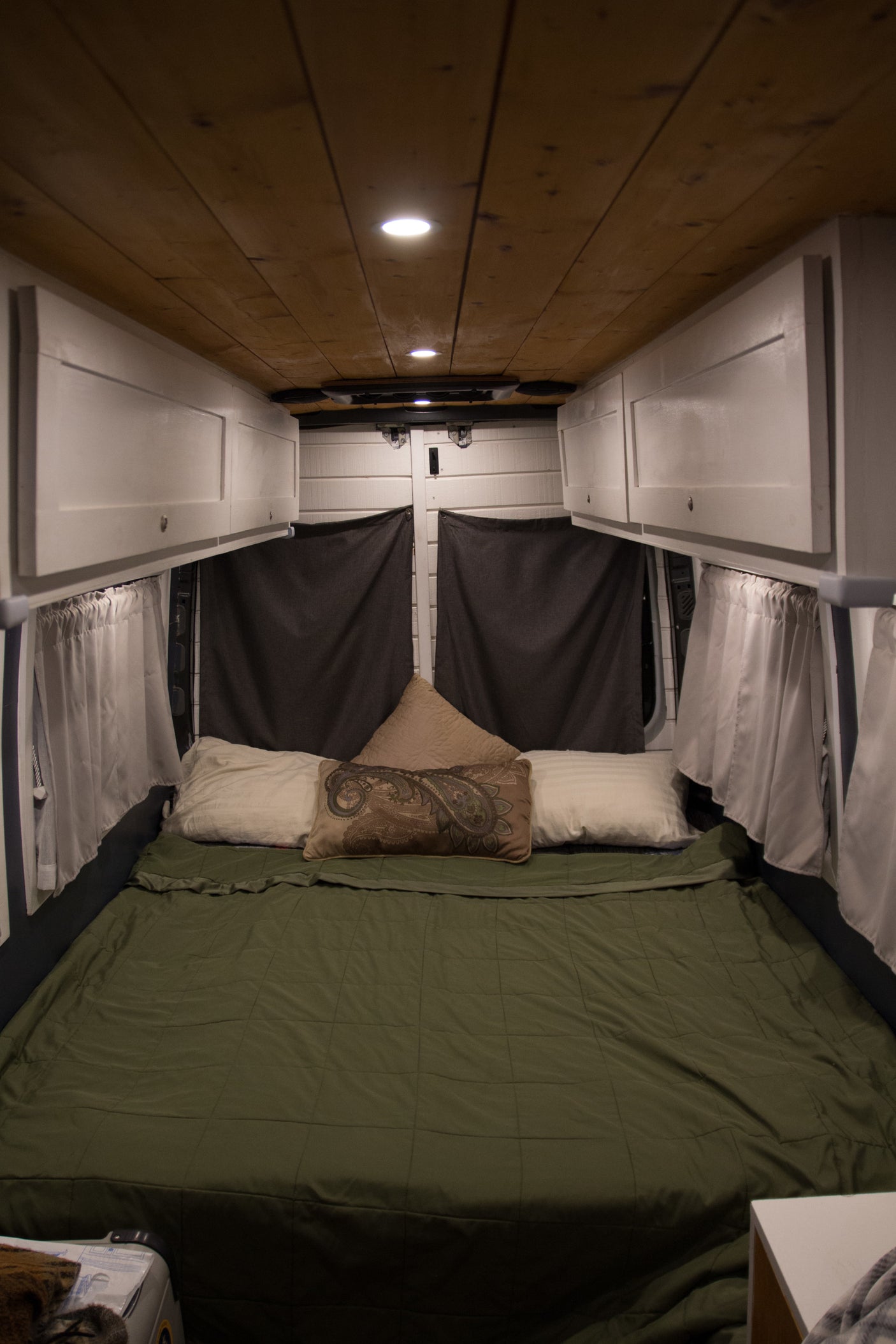 Comfortable RV rental interior featuring a cozy bed, wooden ceiling, custom white cabinets, and blackout curtains.