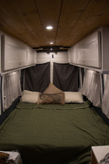 Comfortable RV rental interior featuring a cozy bed, wooden ceiling, custom white cabinets, and blackout curtains.