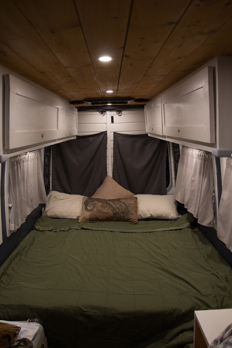 Comfortable RV rental interior featuring a cozy bed, wooden ceiling, custom white cabinets, and blackout curtains.