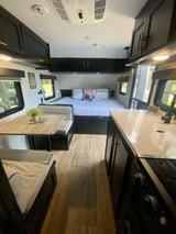 This RV rental interior showcases a compact layout with a cozy bed, a dining area, and a functional kitchen.