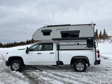 White Chevrolet 2500 HD pickup with a 'FISHHOOK' truck camper on snowy ground, great for an RV rental winter adventure.