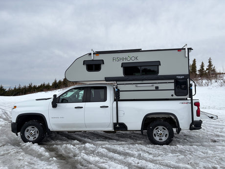 White Chevrolet 2500 HD pickup with a 'FISHHOOK' truck camper on snowy ground, great for an RV rental winter adventure.