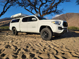 White Toyota Tacoma with a Roofnest rooftop tent. This RV rental is ready for off-road adventures, parked on sand.