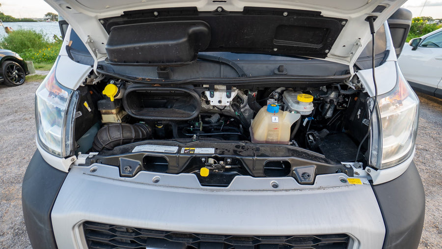 Open hood of a white RV rental van, revealing the engine bay with various fluid reservoirs, wiring, and headlights visible.