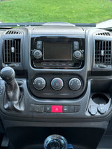 Dashboard of an RV rental: A detailed view of the center console with infotainment screen, climate dials, gear shifter, and power outlets.