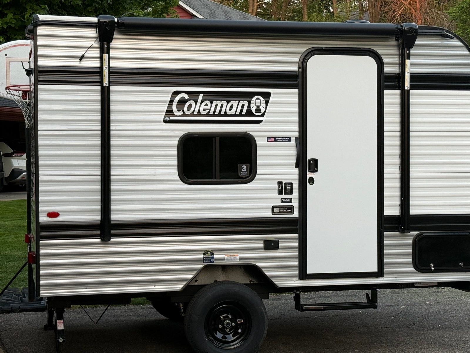 This Coleman RV rental, a striped travel trailer, features a side door, window, and retracted awning, ready for your next adventure.