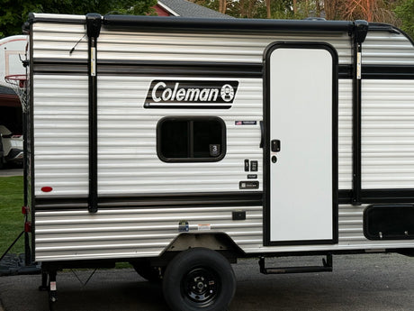 This Coleman RV rental, a striped travel trailer, features a side door, window, and retracted awning, ready for your next adventure.