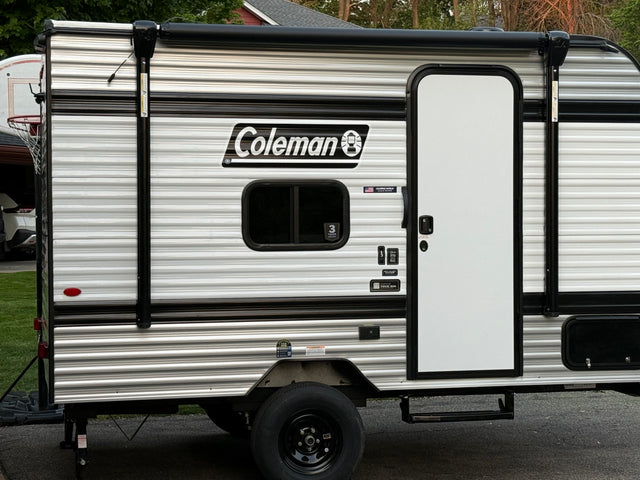 This Coleman RV rental, a striped travel trailer, features a side door, window, and retracted awning, ready for your next adventure.