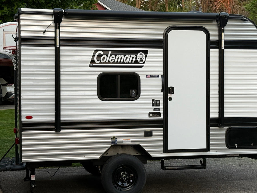 This Coleman RV rental, a striped travel trailer, features a side door, window, and retracted awning, ready for your next adventure.