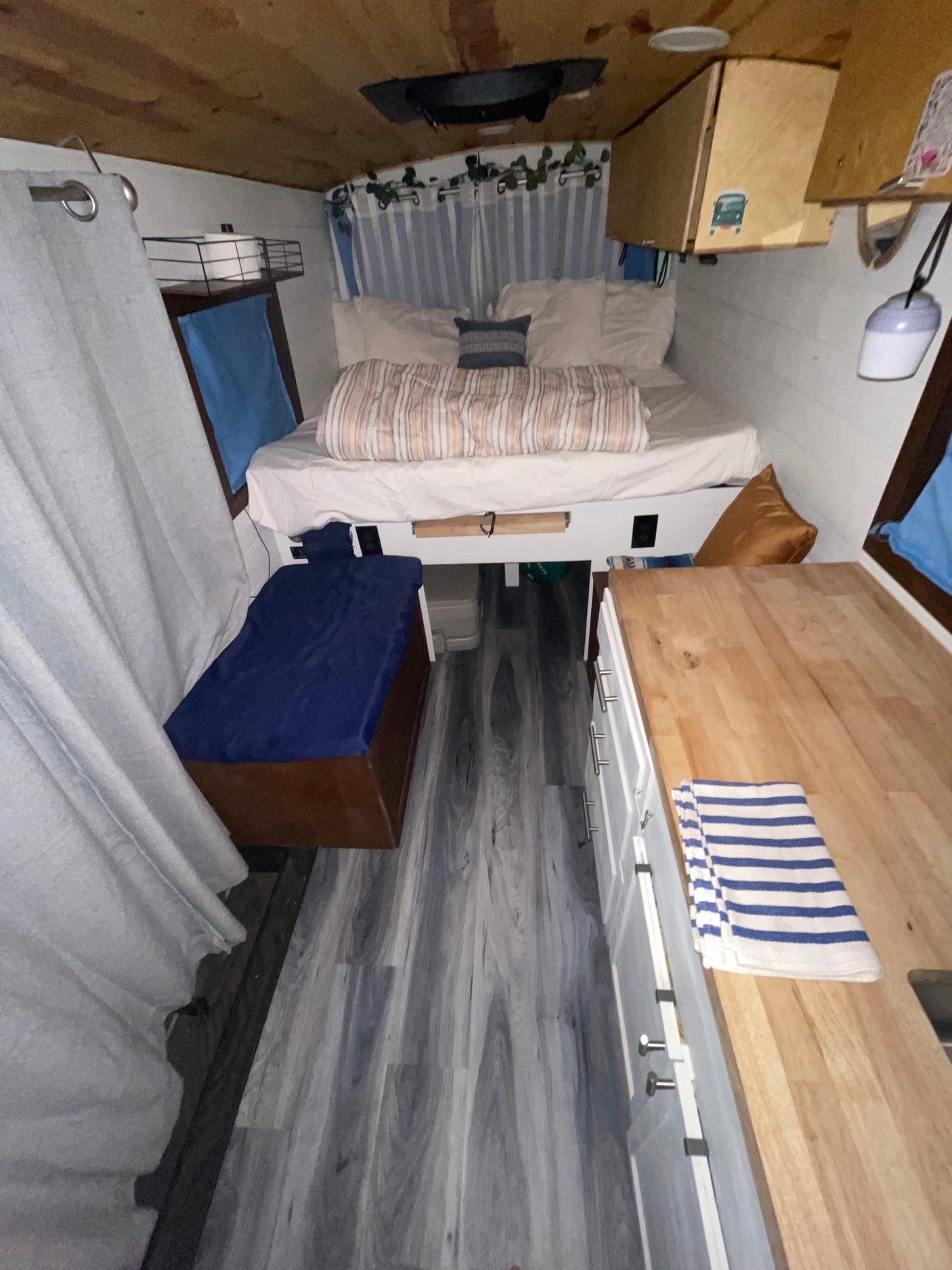 Inside an rv rental: a cozy space with bed, kitchen counter, wood-look floor, & white cabinets.