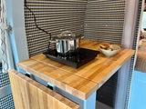 This RV rental kitchen features a light wood counter, induction cooktop with a pot, and a stylish patterned wall.