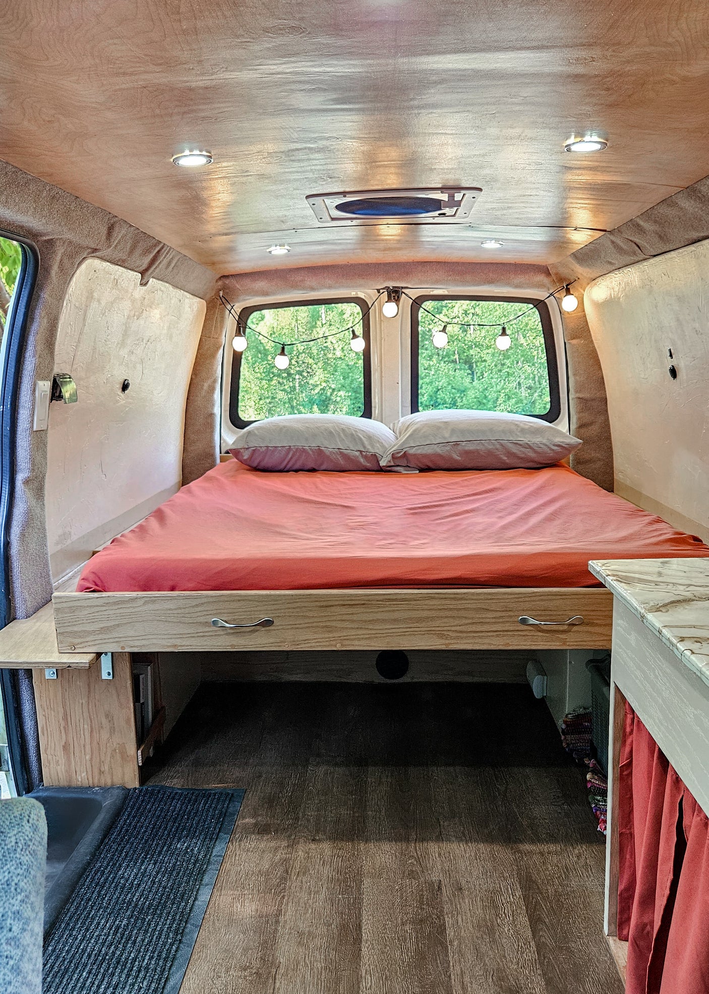 Cozy RV rental bed area featuring custom wood cabinetry, warm lighting, and a view of nature. Perfect for travel.