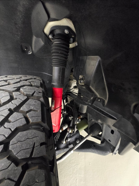 RV rental: Close-up of heavy-duty tire, red shock, and vehicle suspension components in the wheel well.