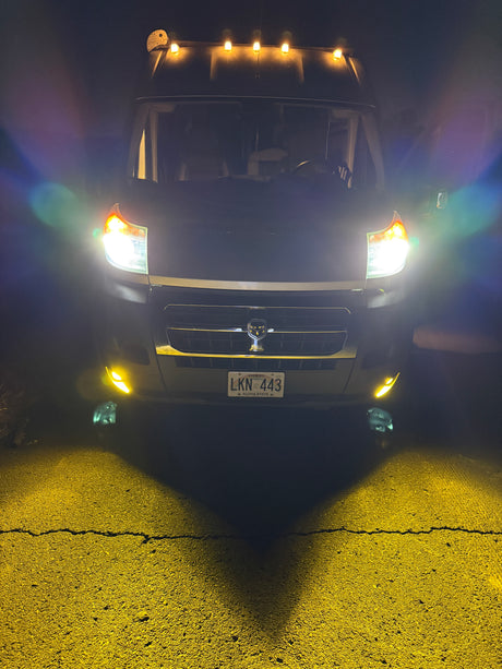 Brightly lit RV rental van at night, showing headlights, yellow fog lights, and roof markers. Hawaii plate LKN 443.
