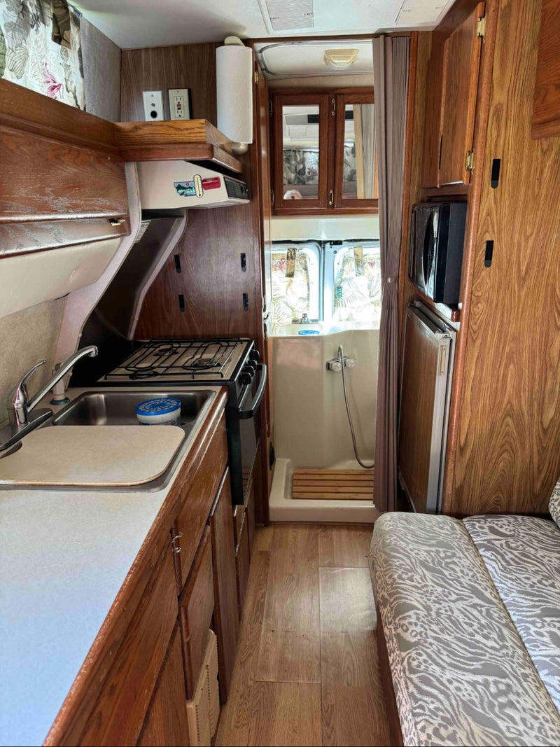 RV rental interior: A compact galley with a sink, stovetop, and microwave, adjacent to a small wet bath and cushioned seating. — photo 15